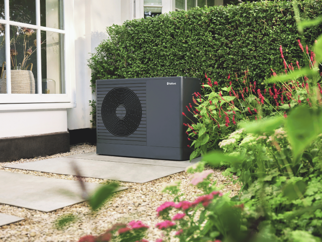 aroTHERM pro in front of a hedge beneath a window.