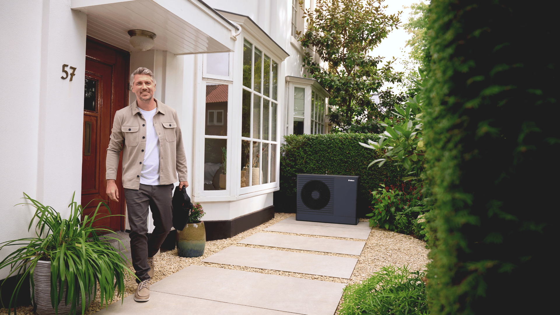 man walking outside his house with an aroTHERM pro heat pump in the background.