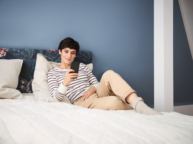 woman sat on her bed looking at her phone