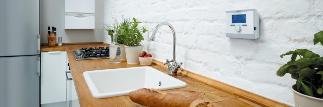 kitchen sink with a boiler and thermostat on the wall. On the kitchen counter there is a loaf of bread that has been cut