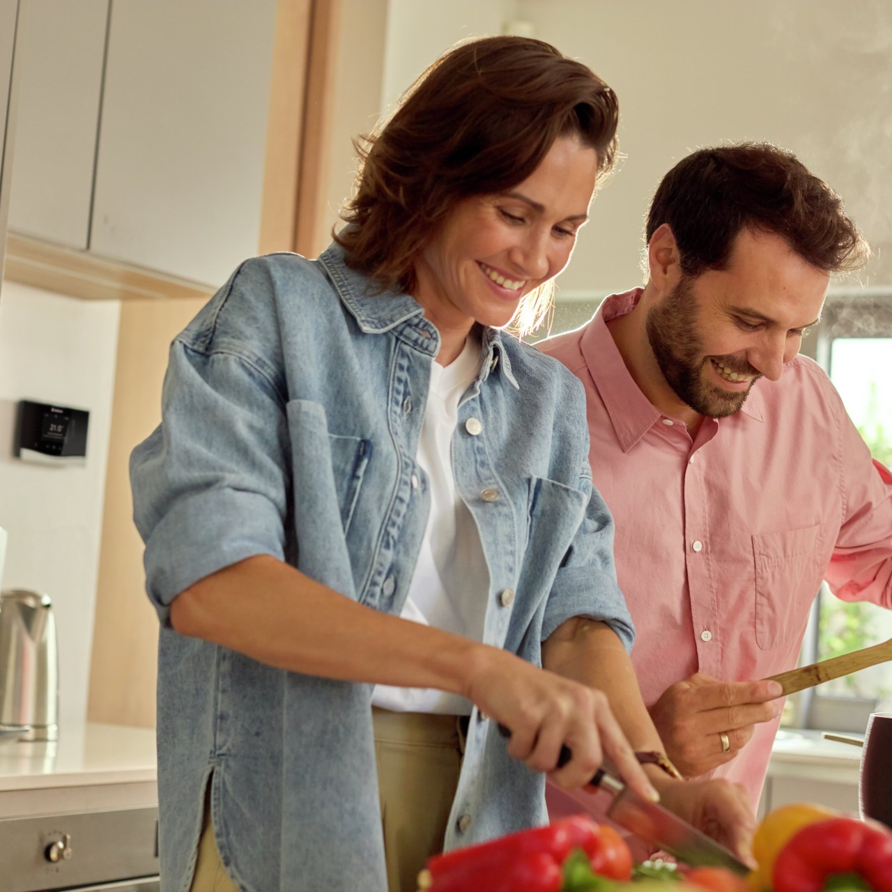 A couple cooking in a kitchen with a control in the background.