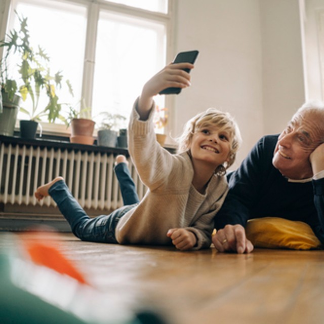 a young boy and man on lying on the floor with the boy taking a selfie on his phone