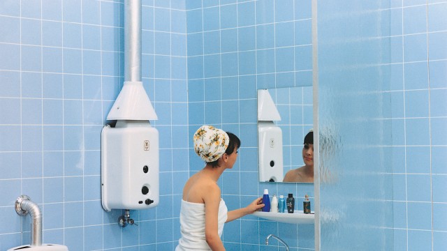 a woman in a towel looking at the mirror in the bathroom with a wall hung boiler on the wall