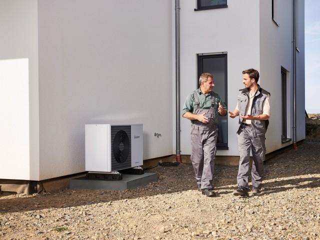 two men walking outside house with a heat pump in the background