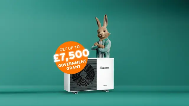 The Vaillant hare standing behind an aroTHERM plus heat pump with an orange circle sticker saying 'Get up to £7,500 government grant'