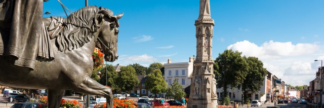 Bronze statue of a figure riding a house with a tall monument next to it 