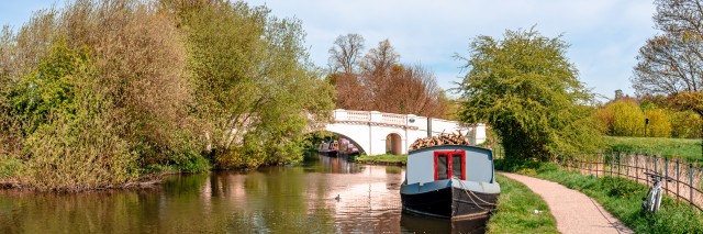 A narrow boat moored at the river Gade, Grand Union Canal. The Grove Bridge aka Grove Ornamental Bridge No 164 is in the background. Cassiobury Park, Watford, England.