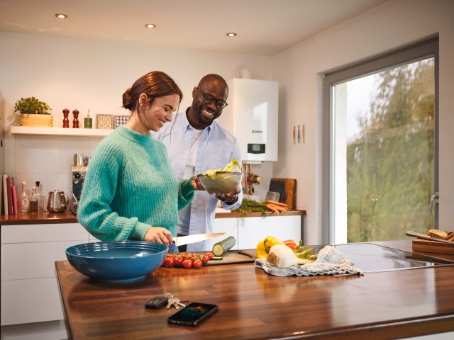 a couple in the kitchen cooking food with a boiler in the background