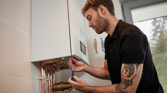 Vaillant installer adjusting pipes underneath an ecoTEC plus boiler on a white wall.