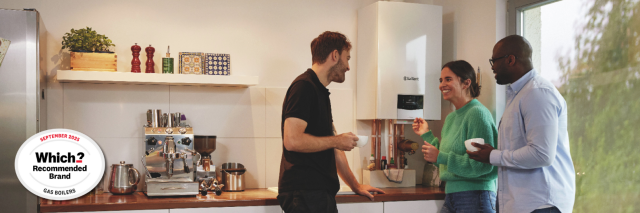 Three people in a kitchen talking with a Vaillant gas boiler on the wall.