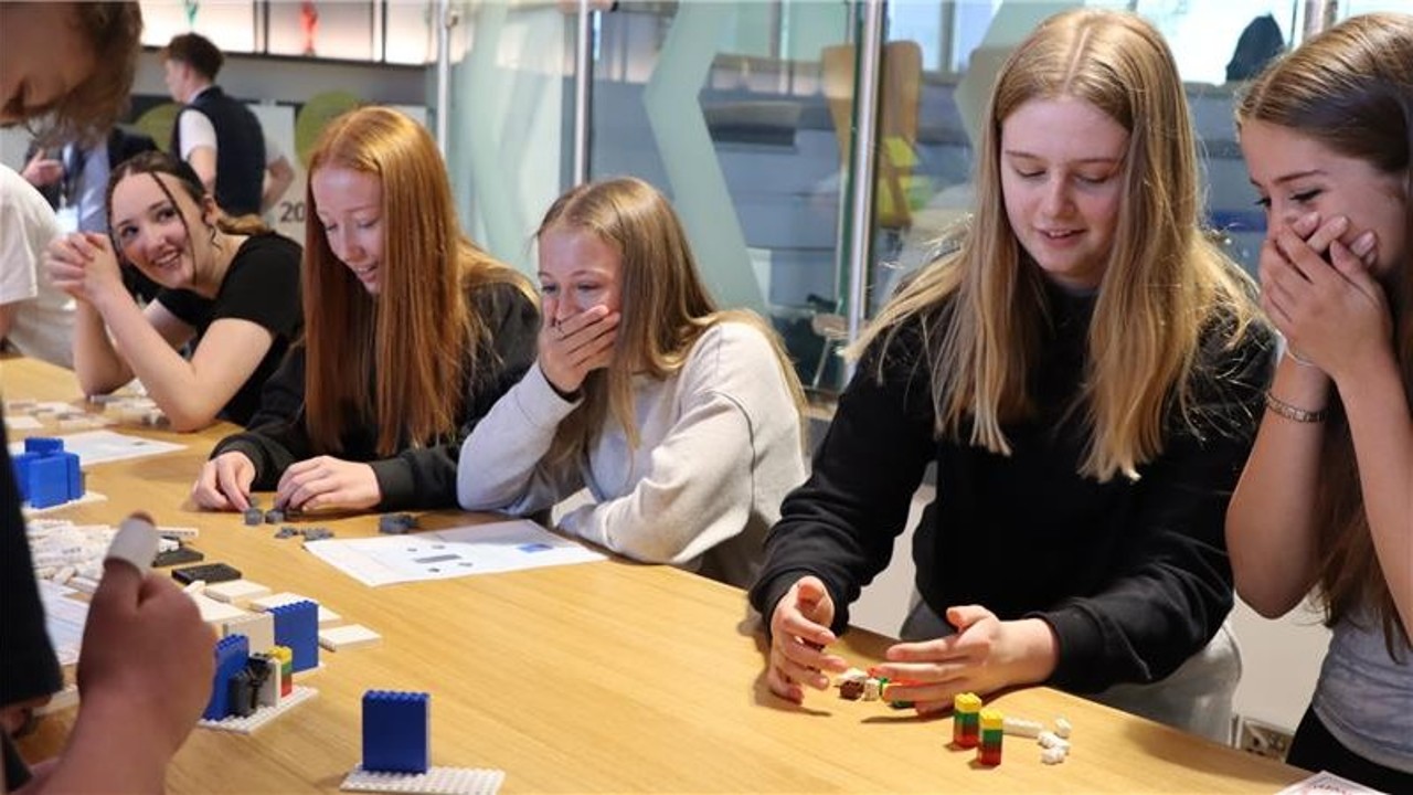 A group of students sat on a table talking and laughing whilst building a lego structure.