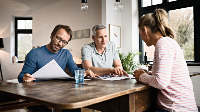 people sat round table talking, man in blue jumper reading 