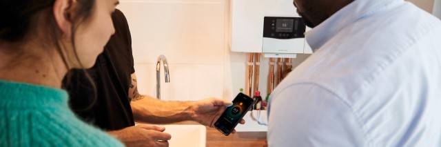 three people looking at a mobile phone with a boiler on the wall