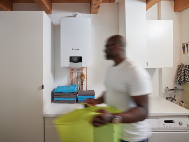 man carrying a green washing basket with a boiler in the background