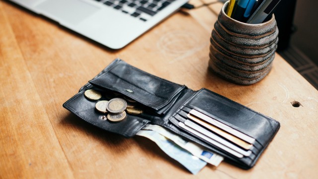 an open wallet with coins falling out and cards in the pockets. Corner of a laptop and a clay pot with pens and pencils