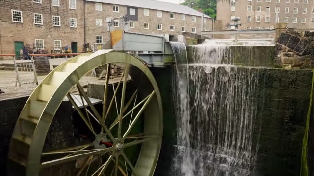  A water wheel is positioned in front of a building, highlighting the blend of nature and architecture in the landscape.