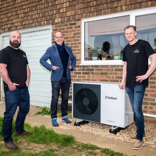 three installers, one being Kevin McCloud standing around a heat pump