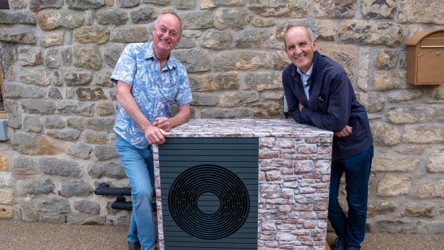 two men leaning against a heat pump that has been wrapped in a brick effect
