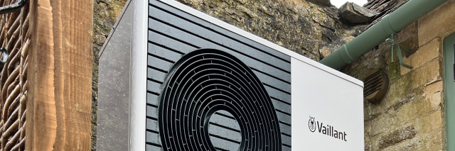 Top view of a heat pump in front of the exterior of a building, showcasing its design and placement.