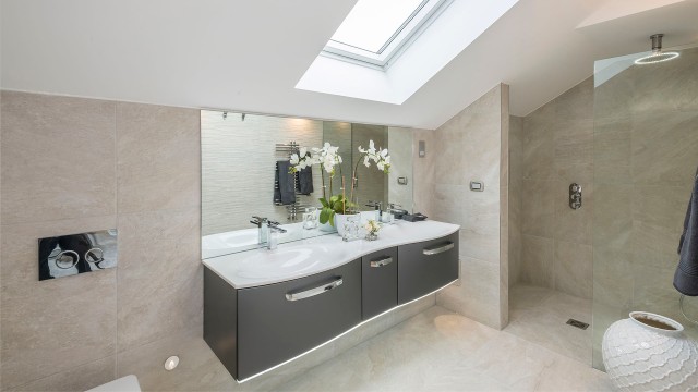 the inside of a bathroom with a walk in shower, a sink with grey cupboards underneath