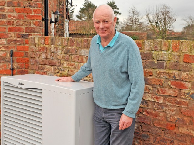 Peter Cliff standing to the right of a heat pump with his left hand on top of it