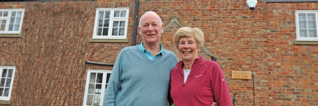 elderly couple standing in front of a brick cottage