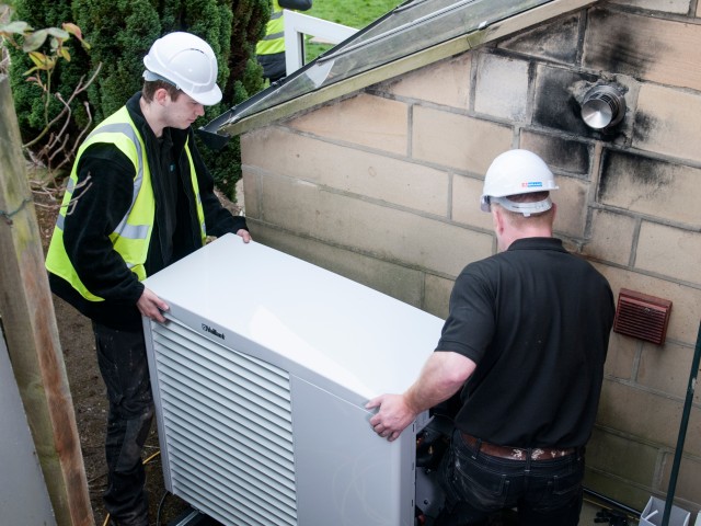 two men with hard hats lifting a heat pump 