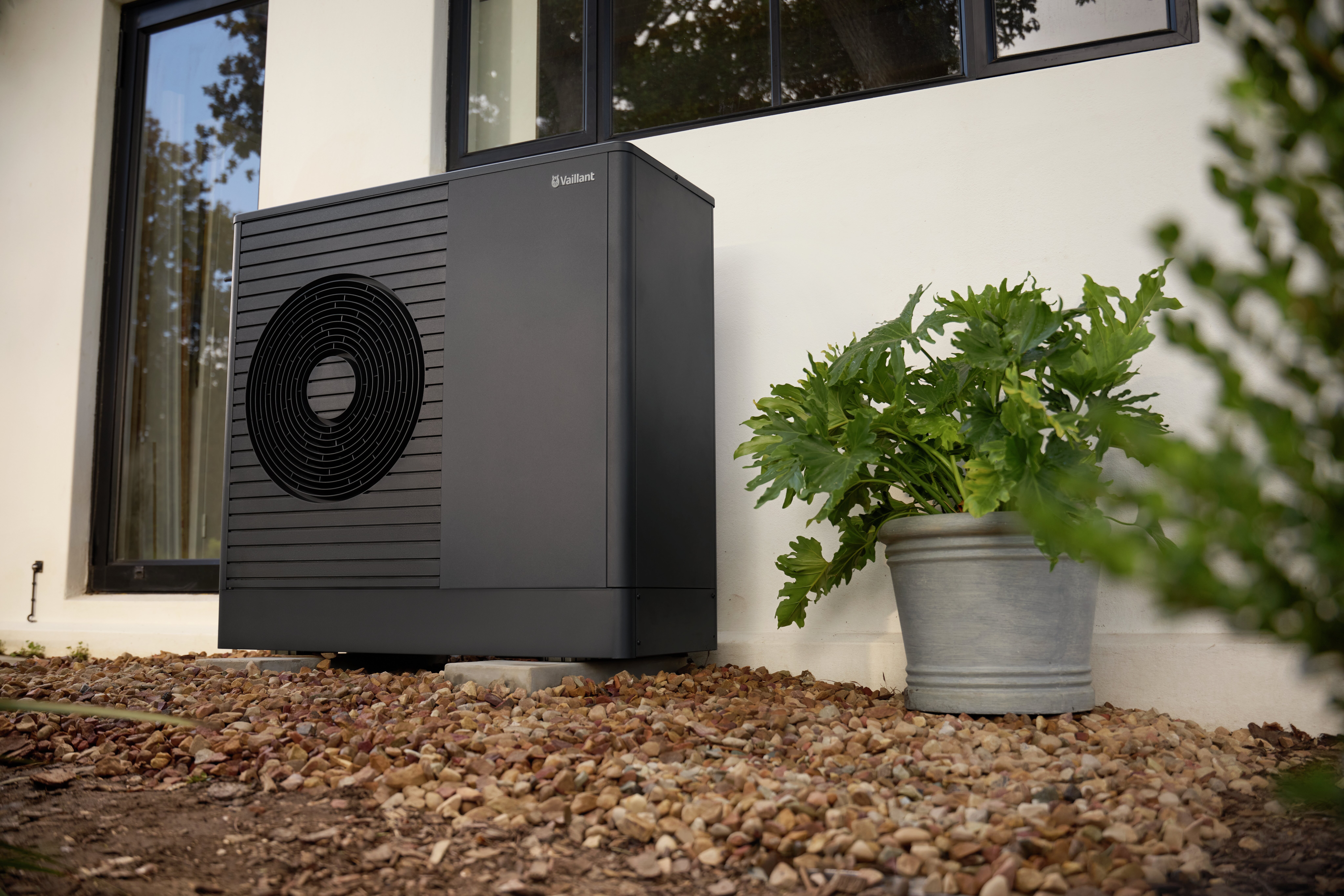aroTHERM plus heat pump in front of a white wall in a garden.