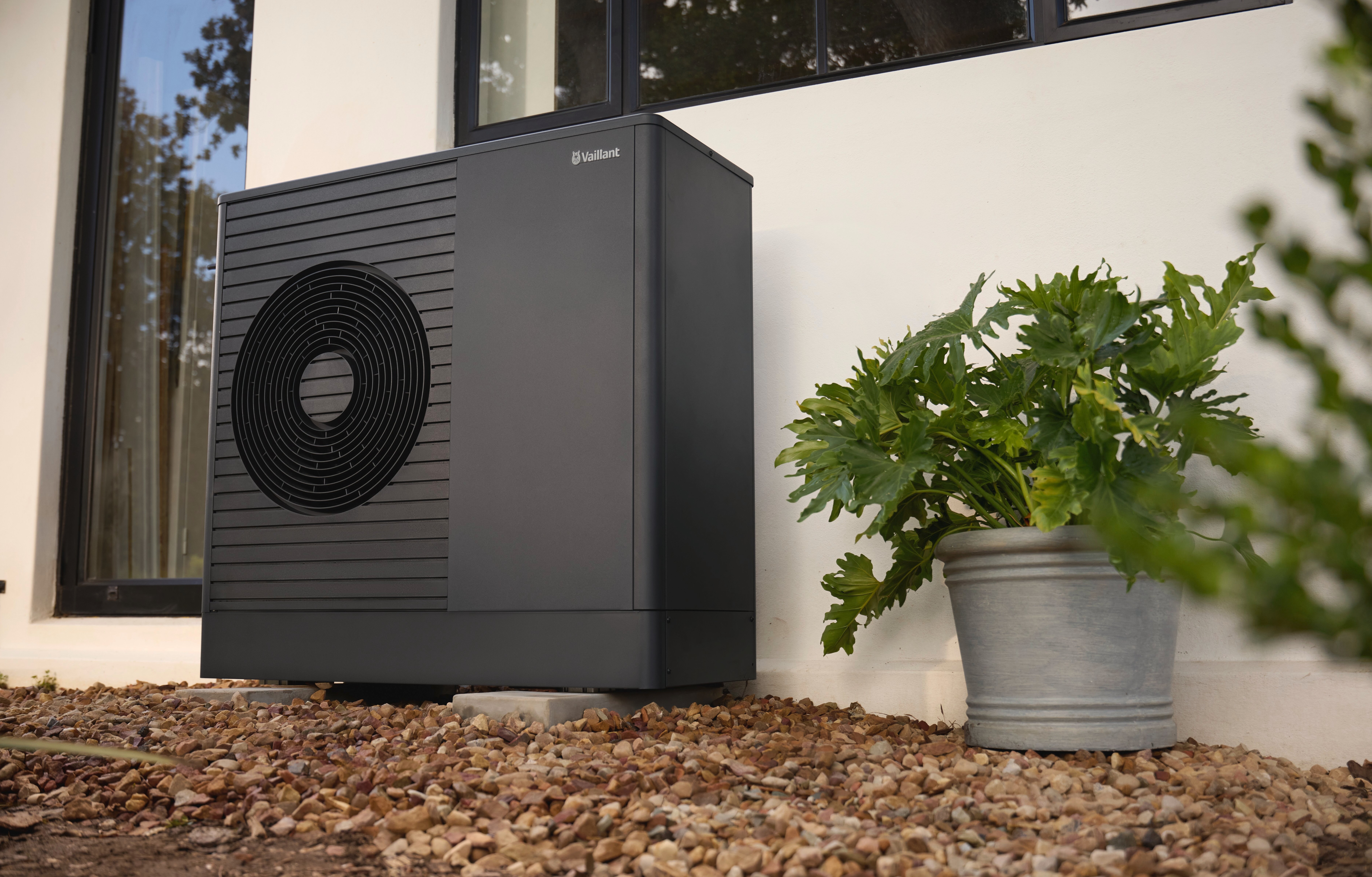 aroTHERM plus heat pump in front of a white wall in a garden.