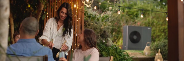 people sat around a table laughing outside, there is an aroTHERM plus heat pump in the background.