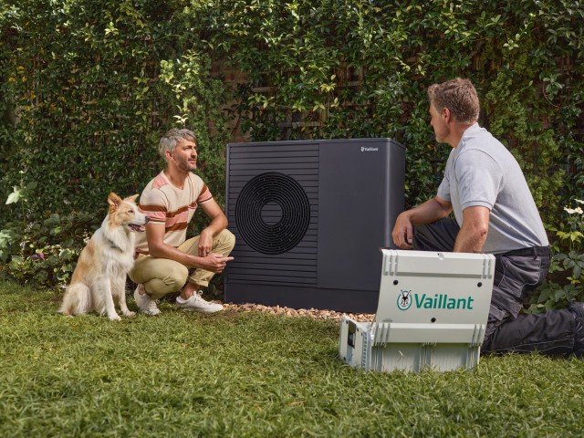 man with a homeowner and dog kneeling down talking in front of a heat pump.