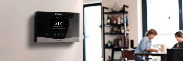 sensoCOMFORT thermostat on wall with people blurred in background