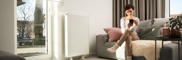 woman sat on a sofa in her living room looking at her phone with a white radiator 