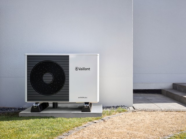 front facing aroTHERM plus heat pump behind a white wall with grass and gravel