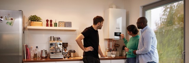 three people in a kitchen looking at a boiler