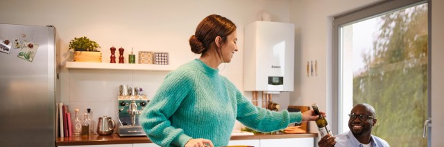 woman in the kitchen, man passing a bottle of wine 