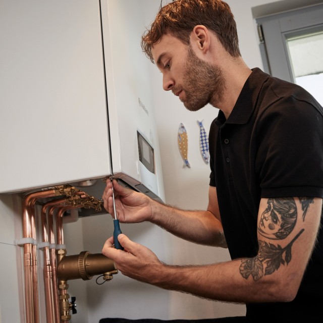 a male installer carrying out some work underneath the bottom of a boiler
