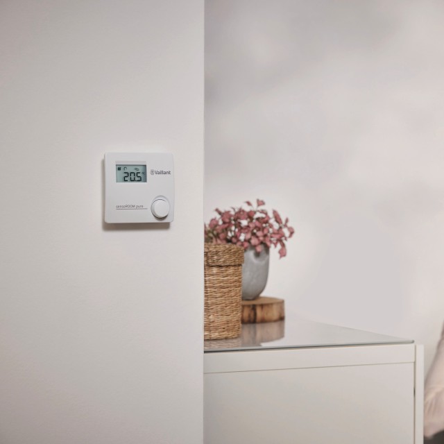 A woman seated in front of a wall-mounted thermostat, adjusting the temperature in her living space.