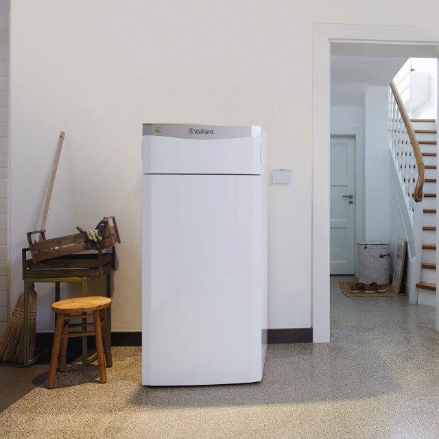 man on his phone stood next to a flexoTHERM heat pump with window in the background