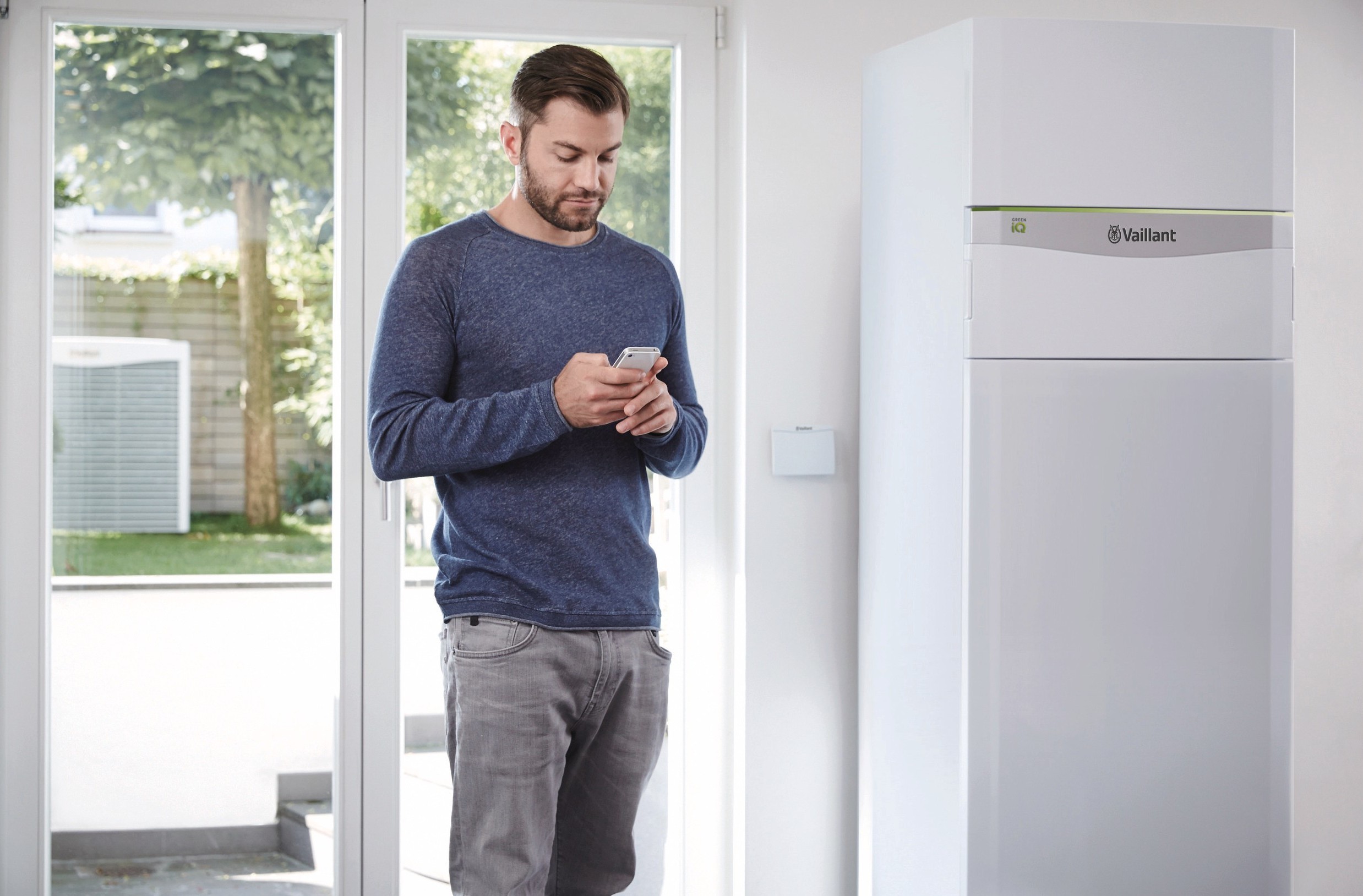 man standing looking at his phone near a large window with the heat pump to the right