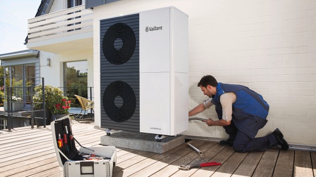 man installing a Vaillant heat pump, he is kneeling down with an open brief case