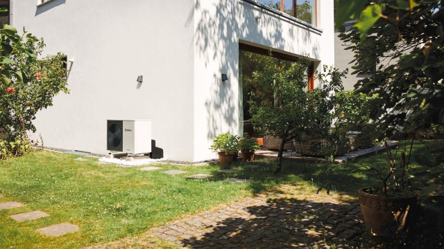 Vaillant heat pump unit in front of a white house with grass in front. 