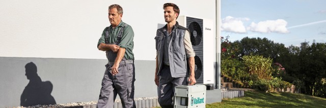 two installers walking in front of the heat pump, one is carrying a Vaillant briefcase 