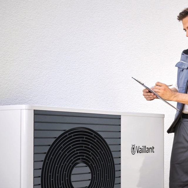 Male installer ho;ding a tablet looking over the heat pump