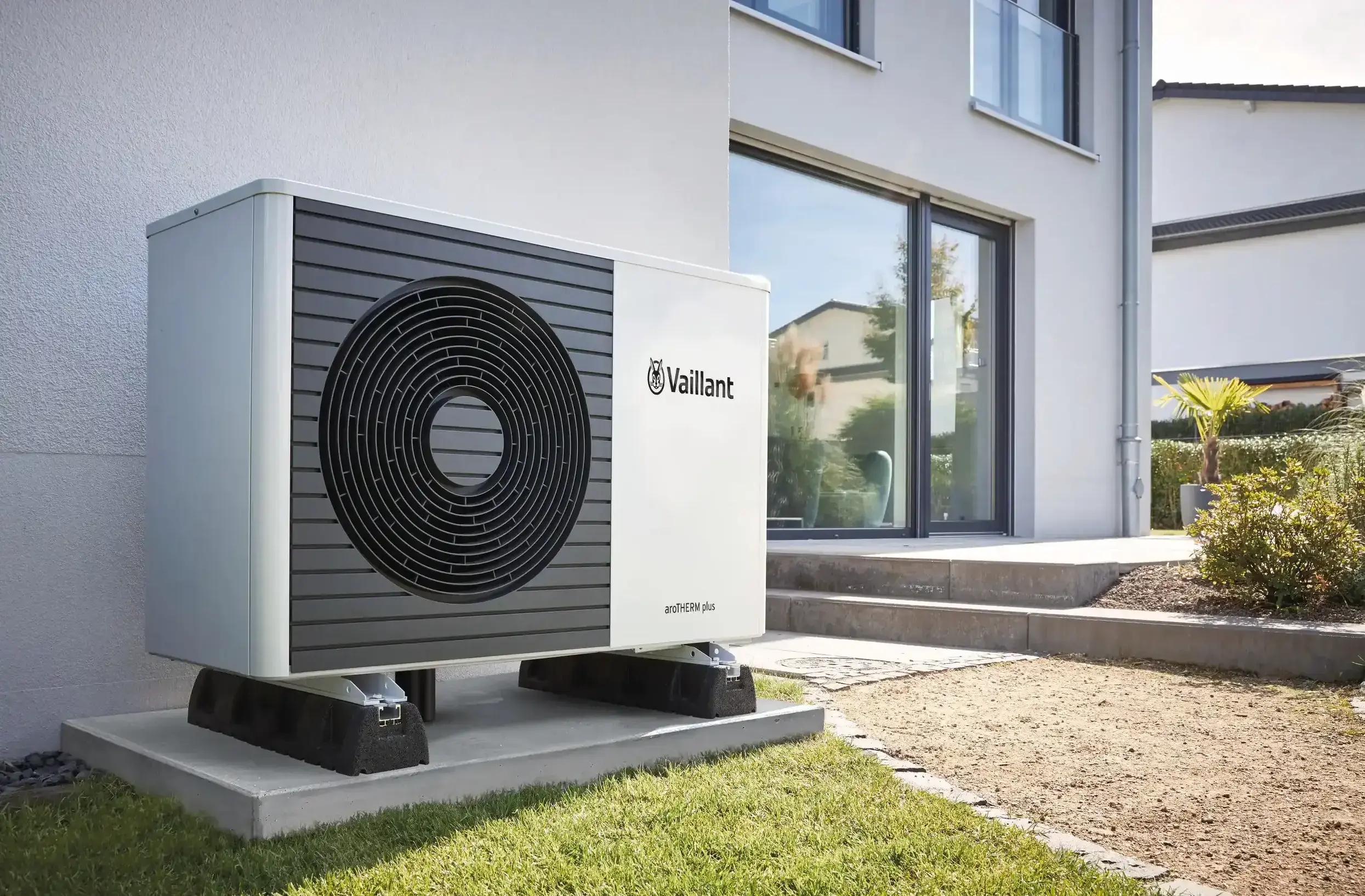 side view of an aroTHEM plus heat pump outside a white brick home