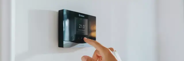side view of a black heating control on a wall with a hand touching the control interface.