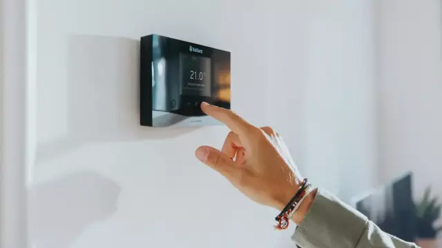 a senso heating control on a white wall with a hand touching the thermostat.