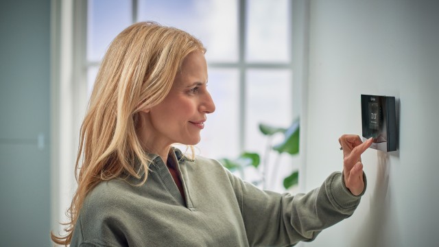a senso heating control on a white wall with a hand touching the thermostat.