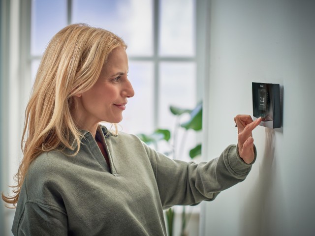 woman turning down a Vaillant thermostat on the wall.