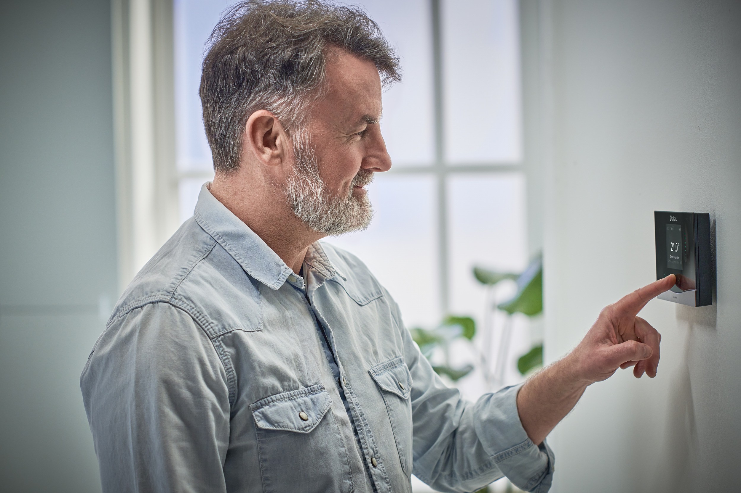A man points to a smart thermostat mounted on a wall, demonstrating its features and functionality.